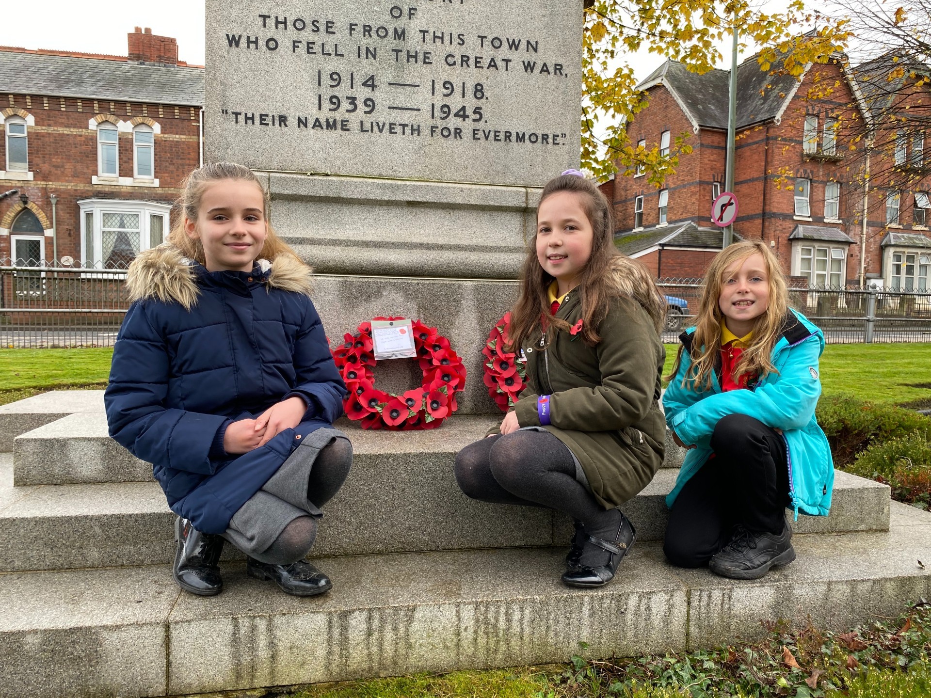 Ysgol Penygloddfa pupils Hollie, Charlotte and Jemima, who have family members serving in the Army and RAF, stand near the poppy wreaths at Newtowns War Memorial. Picture by Anwen Parry/County Times